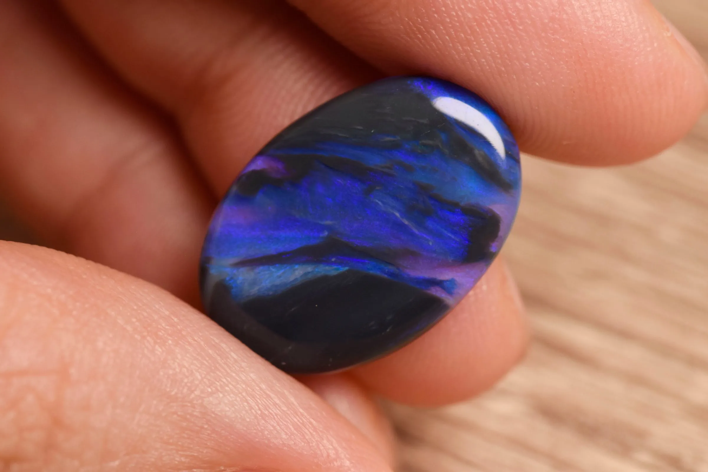 A dark opal held in the hand, deep purple and blue turning within it.